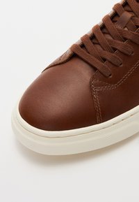 Braune Leder-Sneaker mit glatter Oberflächenbeschaffenheit, runder Zehenpartie, weißer Gummisohle und braunen Schnürdetails. Verfügt über dezente Stichakzente.