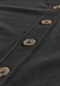 Gros plan sur un tissu gris foncé avec des boutons marron clair visibles le long de la patte de boutonnage, mettant en valeur la texture et le détail des boutons.