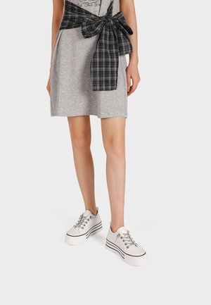 Donna che indossa un vestito grigio alla lunghezza del ginocchio con un fiocco a quadri neri legato in vita e sneaker bianche con suola platform.