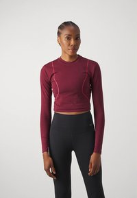 Burgundy long-sleeve crop top with pink stitching details, made of fitted stretch material, paired with black high-waisted leggings.