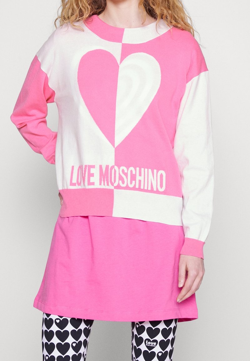 Rosa och vit tröja med en stor hjärtdesign, parat med en rosa kjol och leggings med ett hjärtformat mönster. "Love Moschino" logotypen syns.