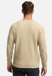 Pull en tricot beige à manches longues, tissu texturé, col rond et détails de ourlet contrastés. Porté avec un pantalon gris foncé.