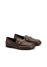 Para brązowych teksturowanych skórzanych mokasynów ze złotym łańcuszkiem, czarnymi, płaskimi podeszwami i zaokrąglonymi noskami, pokazanych na białym tle.