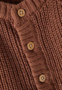 Bruine gebreide cardigan detail met gestructureerd ribbelpatroon en houten knopen met vier gaten. De stof lijkt dik en gezellig.