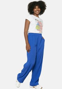 Svetlo modri, nabrani hlače širokega kroja z elastičnim pasom. Kombinirane z belim majico z barvitim grafičnim dizajnom.