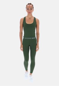 Zöld sportos top és leggings szett, rugalmas anyagból, sima textúrával. Fehér márkás derékszíj és fehér cipők jellemzik.