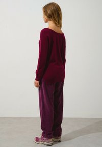 Burgunderröd stickad tröja med vid halsringning, parat med lösa ribbade byxor i matchande färg, samt grå och lila sneakers.