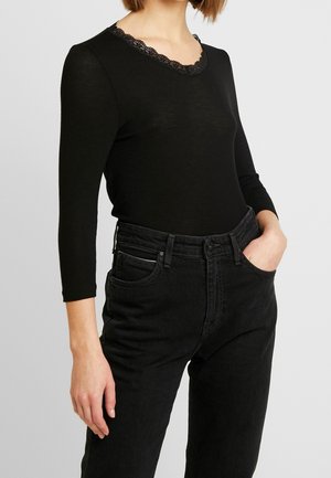 Top nero a maniche lunghe con scollatura in pizzo ondulato, abbinato a jeans neri a vita alta con tasche frontali e vestibilità slim.