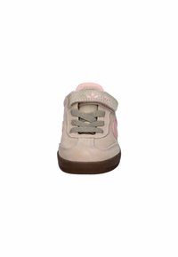 Light beige suede sneaker with pink accents, grey laces, and adjustable strap. Features a textured brown rubber sole. Rounded toe design.
