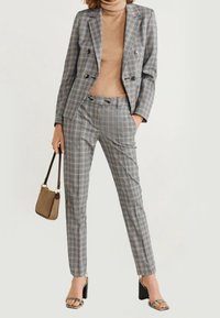 Šedý kostkovaný oblek s dvouřadým sakem a slim fit kalhotami. Texturovaná látka kombinovaná s béžovým rolákem a zelenými sandály na podpatku.