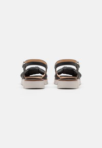 Sandali in pelle nera con una cinghia in pelle marrone e retro texturizzato. Presentano una suola spessa di colore chiaro con scanalature orizzontali.