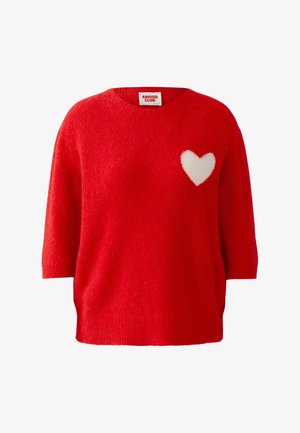 Roter Strickpullover mit lockerem Sitz, kurzen Ärmeln und einem weißen Herzmotiv auf der linken Brust. Strukturierter Stoff mit geripptem Saum.