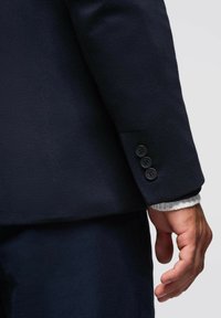 Blazer de lana navy con un ajuste entallado, costuras visibles y detalle de puños de tres botones. Textura suave con un corte moderno.