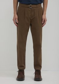 Pantaloni a pieghe marroni con vita aderente e fibbia argentata, abbinati a scarpe marroni stringate, con una texture liscia.