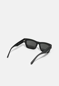 Gafas de sol negras con un diseño de marco geométrico, lentes oscuros, textura mate y un sutil logo de la marca en la patilla.