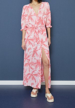 Robe longue en tissu rose clair avec un motif de feuilles de palmier, col en V, manches bouffantes, taille cintrée et fente latérale haute jusqu'à la cuisse.