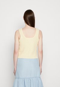 Top de crochê amarelo com bordas dentadas, combinado com uma saia azul clara. Enfoque no tecido texturizado e em detalhes de design simples.