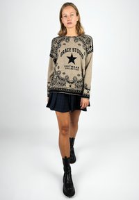 Woman wearing a beige patterned knit sweater with "Grace Studio" text, a short dark plaid skirt, and black platform boots walking forward.