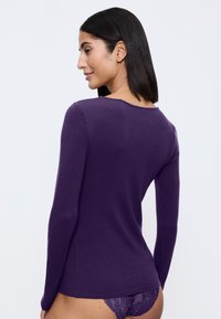 Haut à manches longues violet vu de dos, présentant un col rond et une texture douce et lisse. Accompagné de détails en dentelle sur le sous-vêtement.