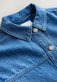 Blue denim jacket collar with metal snap buttons and visible stitching against a plain light background.