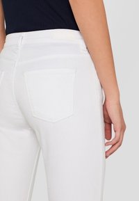 Weiße Denim-Jeans mit einer anliegenden Passform, ausgestattet mit einer Gesäßtasche und einer glatten Textur. Der Bund ist schlicht und passt zur Farbe des Stoffs.