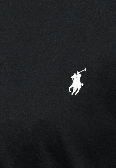 Λευκό κεντητό λογότυπο παίκτη πόλο που ιππεύει άλογο και κουνάει ένα σφυρί σε μαύρο ύφασμα.