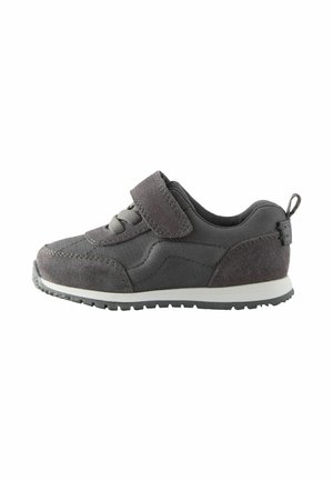 Donkergrijze kindersneaker met klittenbandsluiting, veters, witte zool en een trekband aan de hiel, zijaanzicht getoond op een witte achtergrond.
