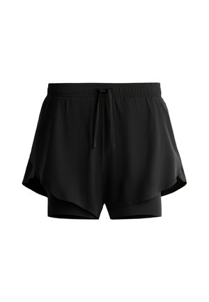 Femme portant des lunettes de soleil noires, un t-shirt blanc oversize par-dessus des manches longues à rayures noires et blanches, un short noir, des chaussettes blanches et des baskets beiges.