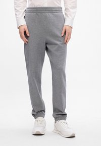 Pantalones de chándal grises hechos de tela suave, con cintura elástica, piernas ajustadas y puños acanalados. Combinados con zapatillas blancas.