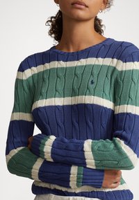 Suéter tejido de cable en azul y verde con rayas horizontales en crema y verde. Puños y dobladillo acanalados, cuello redondo y tejido texturizado.