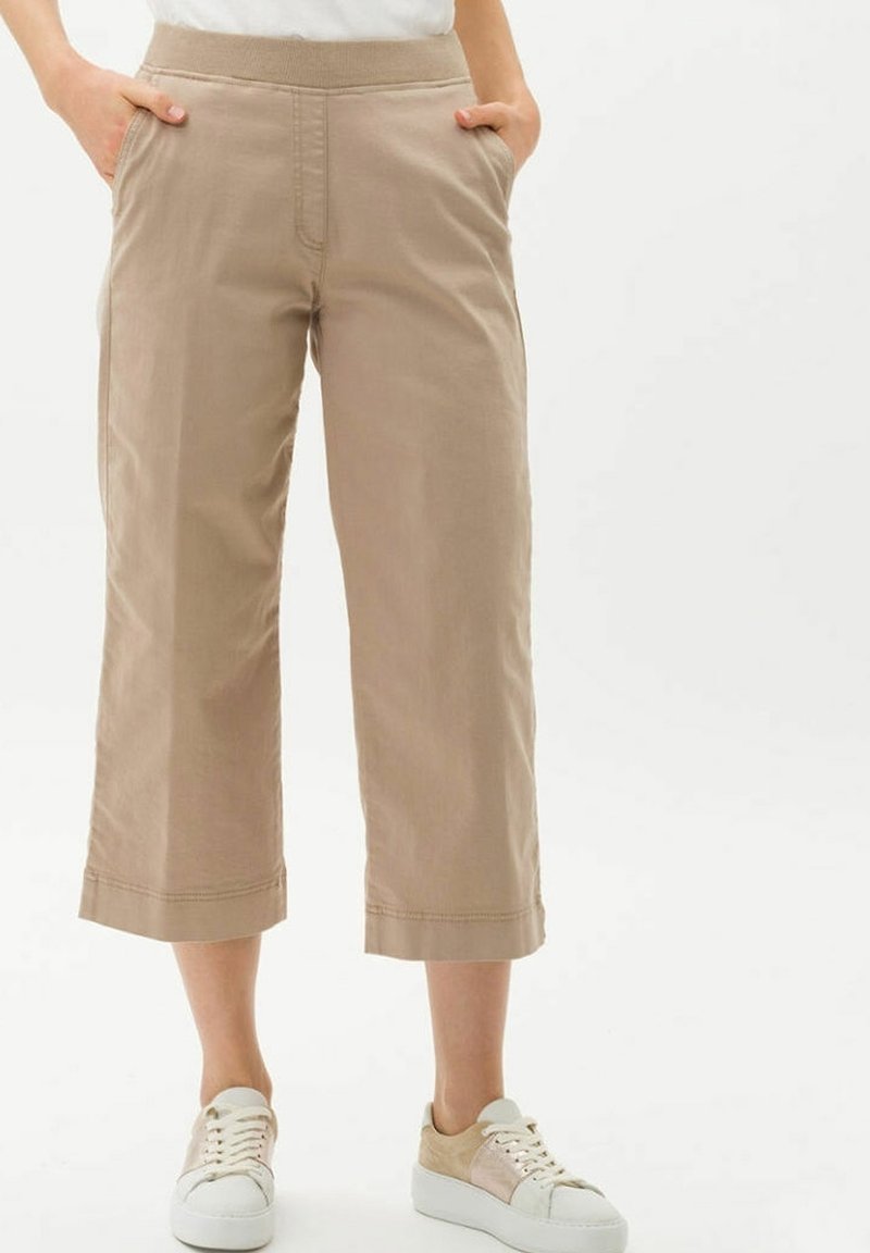 Pantalon beige large et court avec taille élastique, poches avant, porté avec des baskets basses blanches et beiges.