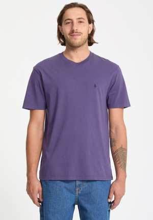 Paarse katoenen t-shirt met korte mouwen en een ronde hals. Bevat een klein zwart logo op de borst. Draagt met blauwe denim jeans.