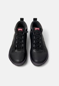 Zapatillas altas de cuero negro con una superficie texturizada, que cuentan con cordones negros, una etiqueta de marca roja y una suela de goma.