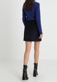 Mini-jupe en velours côtelé noir à coupe droite, associée à un pull bleu. Bottines noires à finition brillante et talons épais.