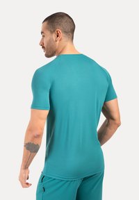 Szmaragdowa sportowa koszulka z krótkim rękawem, wykonana z gładkiego, lekkiego materiału. Posiada okrągły dekolt oraz raglanowe rękawy, zestawiona z dopasowanymi szmaragdowymi spodniami.