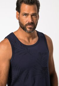 Námořnická modrá tílko vyrobené z bavlny, s jemným vzorem listů, kulatým výstřihem a malou kapsičkou na levé straně hrudníku. Hladký povrch.