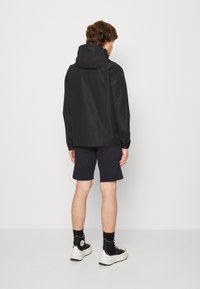 Zwarte waterdichte jas met een capuchon, ontworpen met een gladde textuur, gecombineerd met marineblauwe shorts en zwarte hoge sneakers.