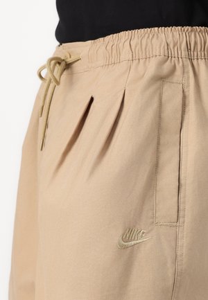 Shorts Nike beiges avec une taille élastique dotée d'un cordon de serrage, des plis sur les côtés, et un petit logo brodé sur la jambe gauche.
