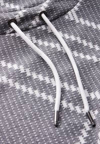 Grau-weiß gemusteter Stoff mit sichtbarem Kordelzug, ausgestattet mit Metallösen und strukturiertem Strickdesign, das ein geometrisches Muster zeigt.