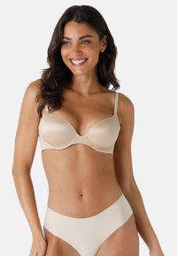 Reggiseno push-up senza cuciture con tessuto liscio, coppe sagomate e spalline regolabili; abbinato a slip senza cuciture in un leggero colore beige.
