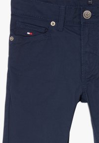 Granatowe bawełniane spodnie z przednią kieszenią, małym logo w czerwono-biało-niebieskich kolorach, metalowym guzikiem i kontrastowymi szwami.