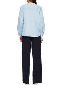 Lichtblauwe blouse met ballonmouwen, geplooide details aan de achterkant, gecombineerd met marineblauwe broek met een wijde pijp en contrasterende manchetten.
