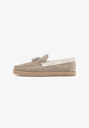Suede loafers in taupe with cream accents, a braided jute sole, decorative stitching, and a small decorative tassel on the upper.