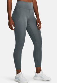Leggings grigi con vita alta, dotati di tasche laterali e realizzati in un tessuto liscio ed elastico. Il design include dettagli di texture sottili.