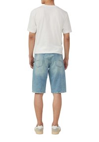 Witte katoenen t-shirt gecombineerd met lichtblauwe denim shorts. De shorts hebben een relaxte pasvorm en details van stiksel op de achterzak. Sneakers met rubberen zolen.