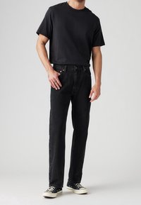 Black t-shirt with short sleeves paired with dark jeans. Shoes are black with white accents. Simple, casual design, cotton fabric.