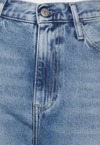 Jeans in denim blu chiaro con vita alta, dotati di chiusura a bottoni, lievi segni di scolorimento e cuciture visibili lungo le cuciture.
