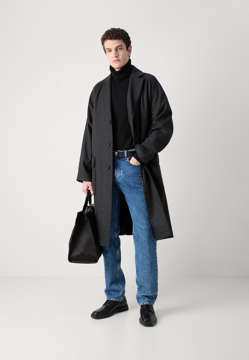 Un long manteau en laine gris, un turtleneck noir, un jeans bleu, des chaussures noires et un sac fourre-tout noir. Le manteau présente de grands boutons et une coupe ample.