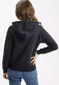 Czarna bluza z kapturem na sznurek, ze ściągaczami u mankietów i na dole. Wykonana z gładkiego materiału, w luźnym kroju, zestawiona z niebieskimi dżinsami.