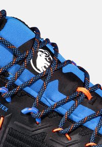 Blå och svarta vandringsskor med en texturerad yta, utrustade med orange och blå snören, samt en logotyp av ett stiliserat djur på tungan.